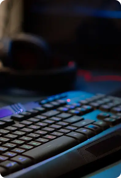 Zbliżenie na klawiaturę gamingową z RGB podświetleniem w ciemnym pokoju, rozmyte tło stanowiska gamingowego